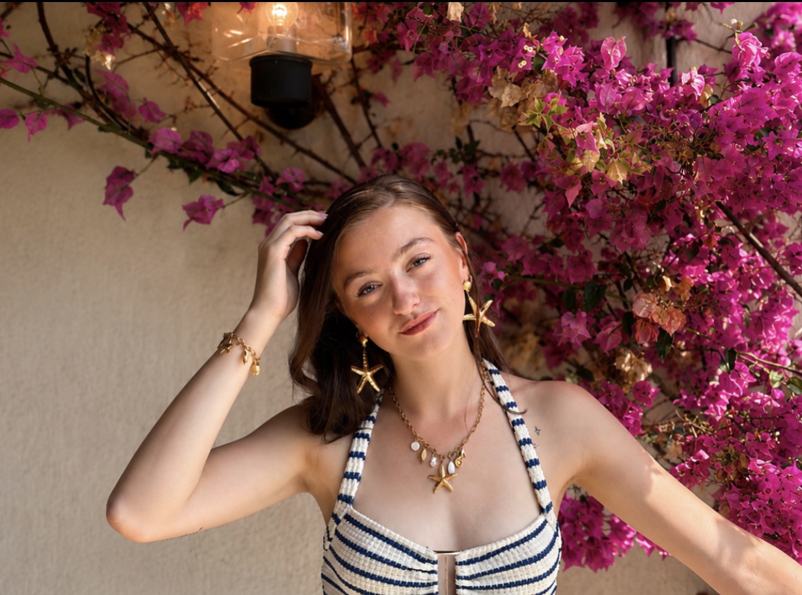 Femme portant des boucles d'oreilles et un collier étoile de mer dorés devant un mur de bougainvillées roses